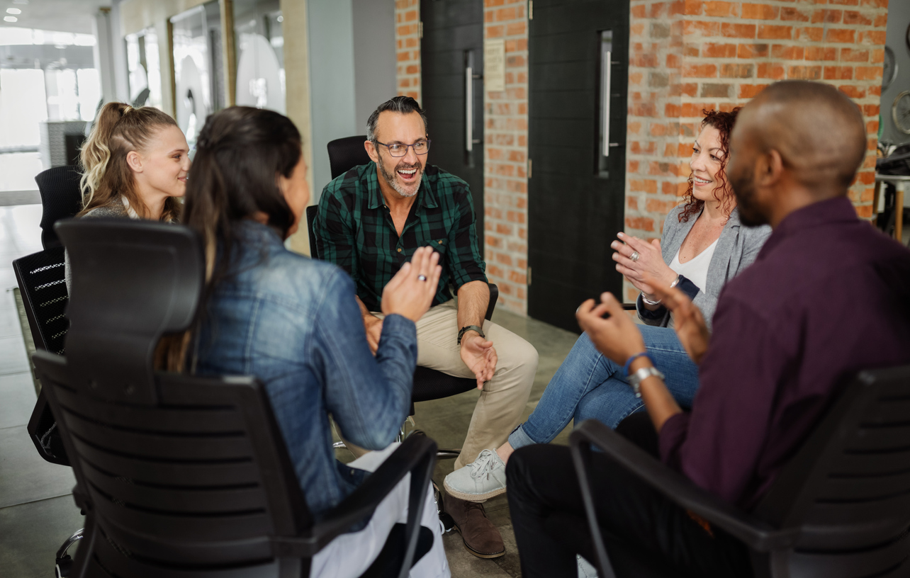 Diverse group of business people sitting in circle. Leader talking with coworkers in a team building session.