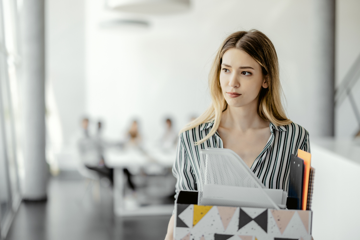 Upset businesswoman with cardboard box of things leaving office after quitting