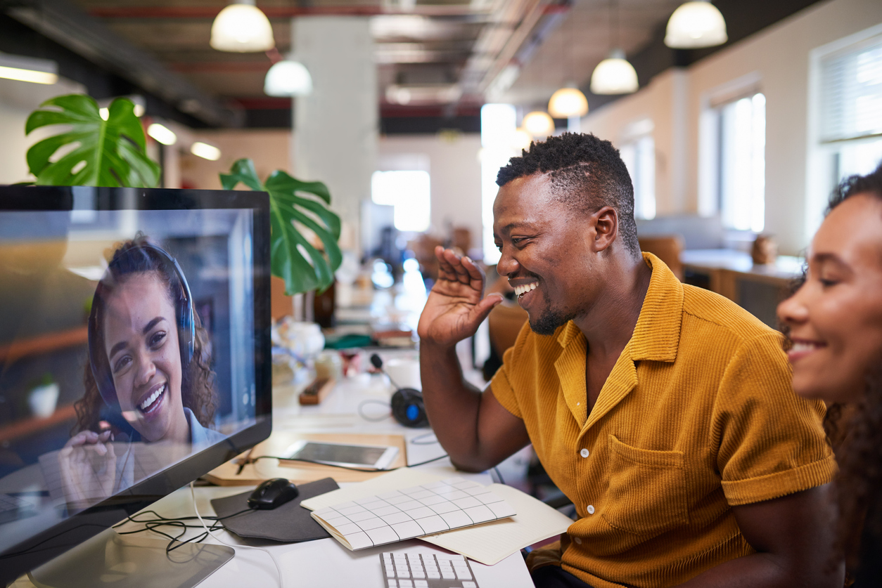 A Black man waves to his colleague on a video call from his office.