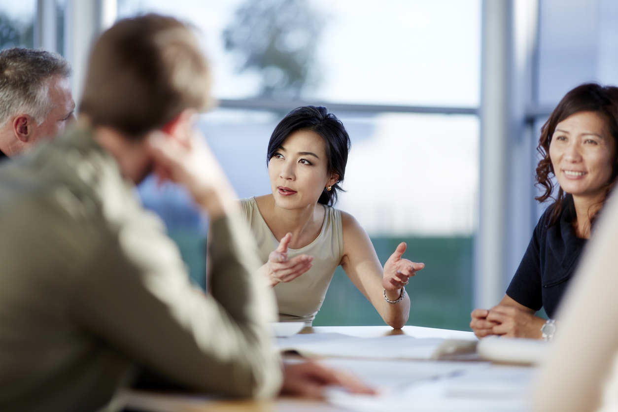 Asian female leader, speaking to business people talking in meeting.