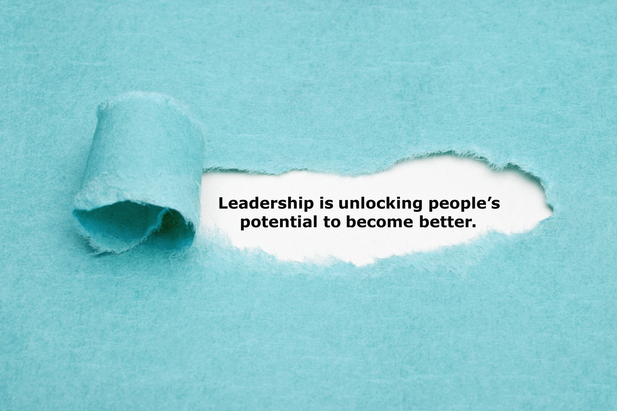 Motivational quote Leadership is unlocking peoples potential to become better appearing behind torn blue paper.