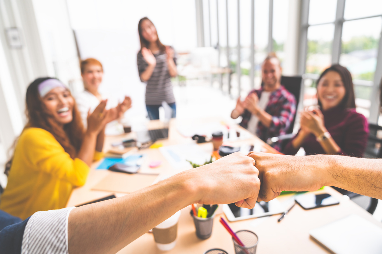 Business partners or coworkers fist bump in team meeting.