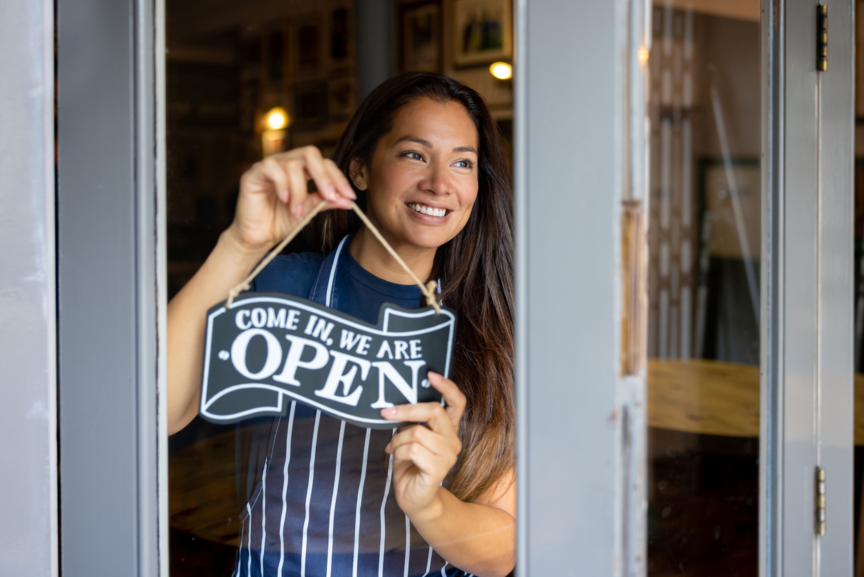 Happy waitress working at a pub and hanging an open sign.