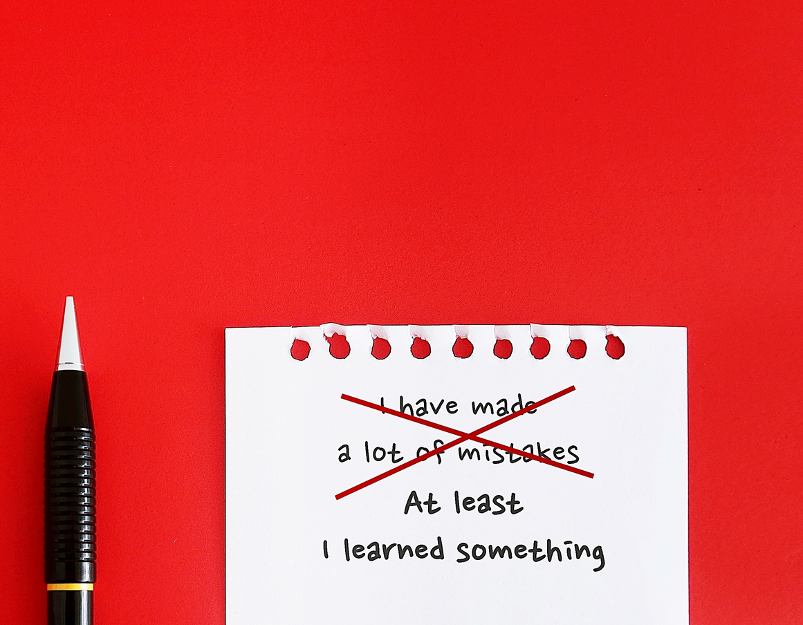 On red copy space background, pencil writing on paper I HAVE MADE A LOT OF MISTAKES, replaced with AT LEAST I LEARNED SOMETHING – to challenge pessimistic self-talk by reframe negative thoughts to positive thinking and increase self-confidence Changing Perspective - Emotional Intelligence Thought